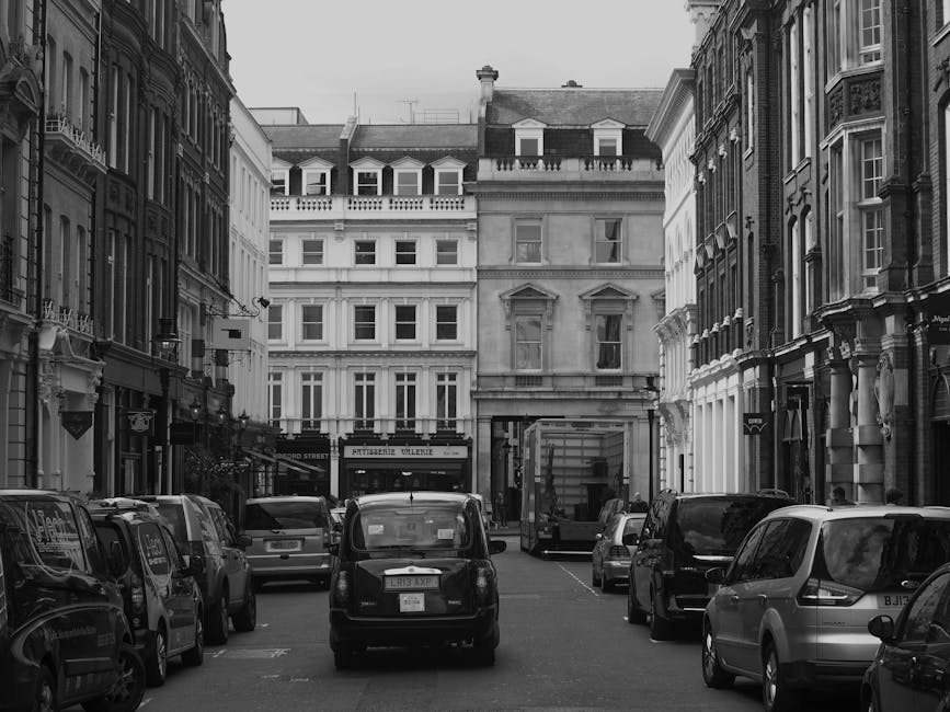 A narrow residential street with a paved pathway surrounded by multi-storey brick and white-painted buildings. On the left, there is a low brick wall with a metal railing on top, and behind it, a smal